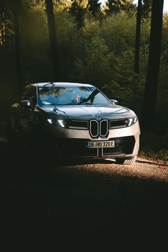BMW iX3 mit Scheinwerfern im dunklen Wald