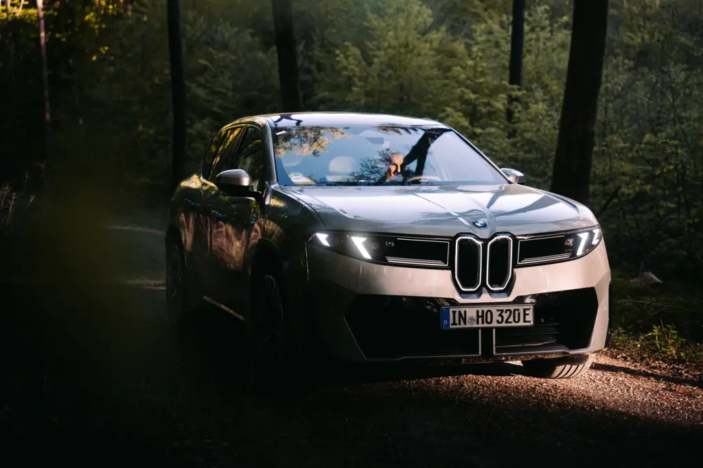 BMW iX3 mit Scheinwerfern im dunklen Wald