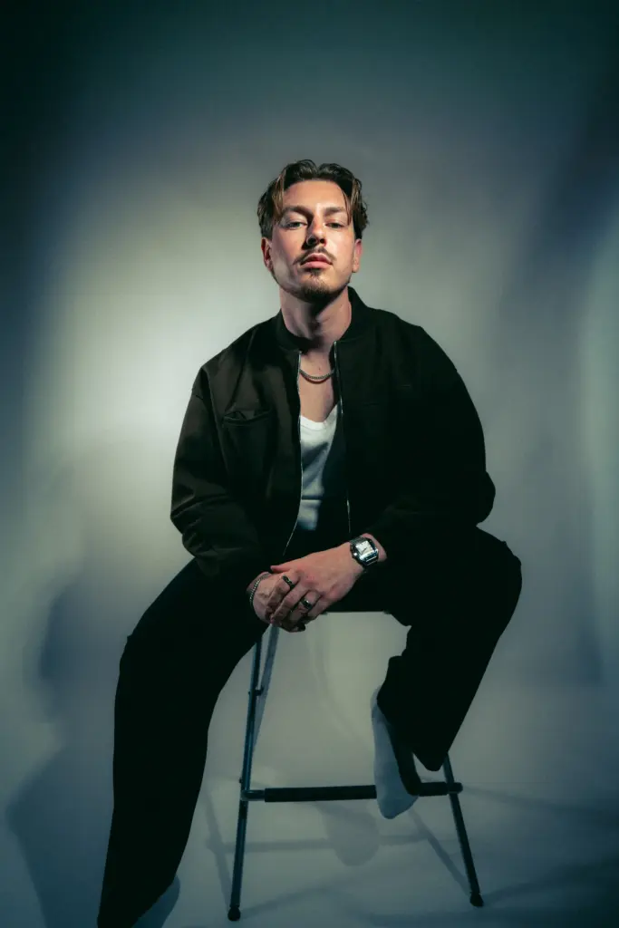 DJ Wamax in Schwarz auf einem Hocker