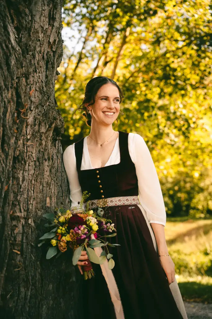 Braut im Dirndl mit Brautstrauß an einem Baum