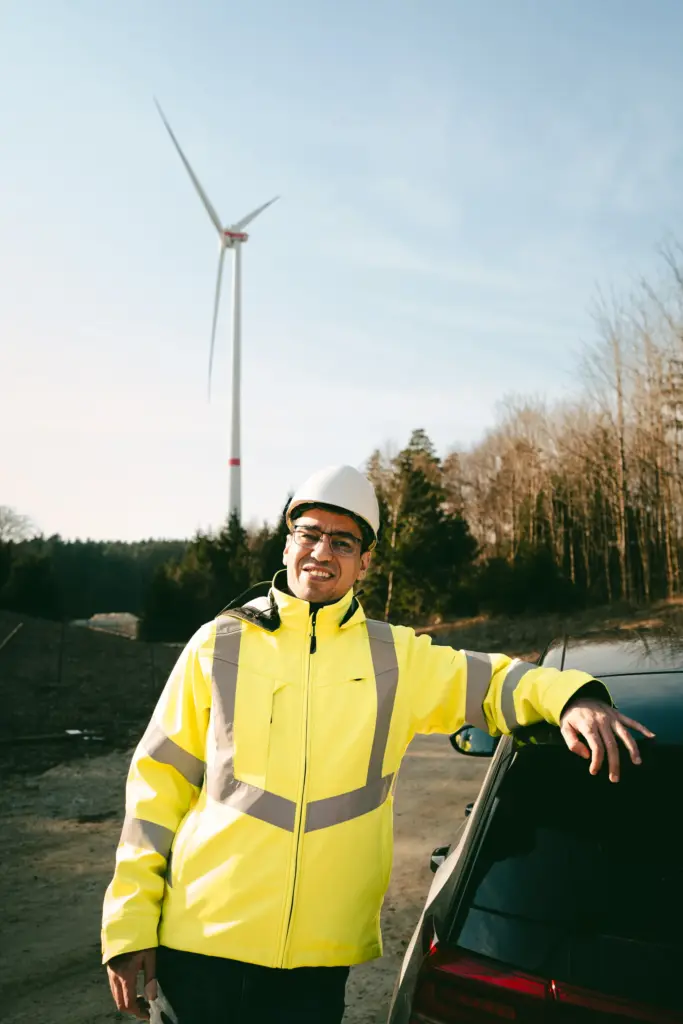 Lachender Mitarbeiter in Warnjacke vor einem Windrad