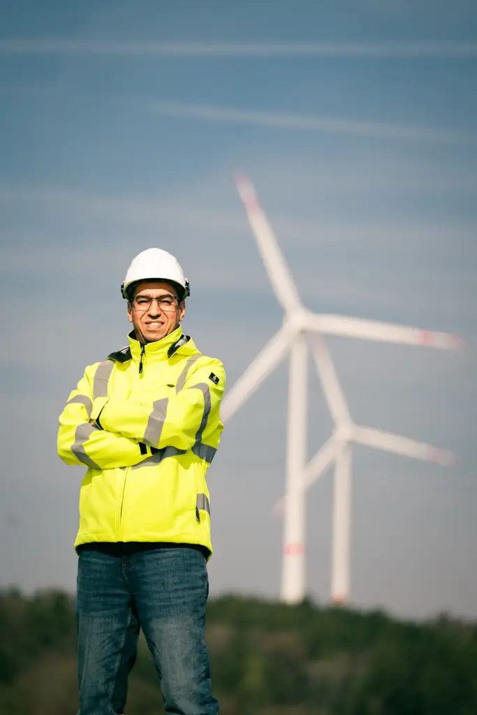 Mitarbeiter in Warnjacke und Helm vor Windrädern