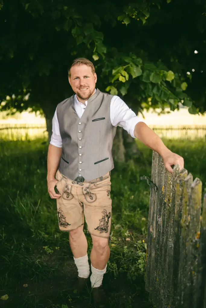 Mann in Lederhose und Weste am Holzzaun